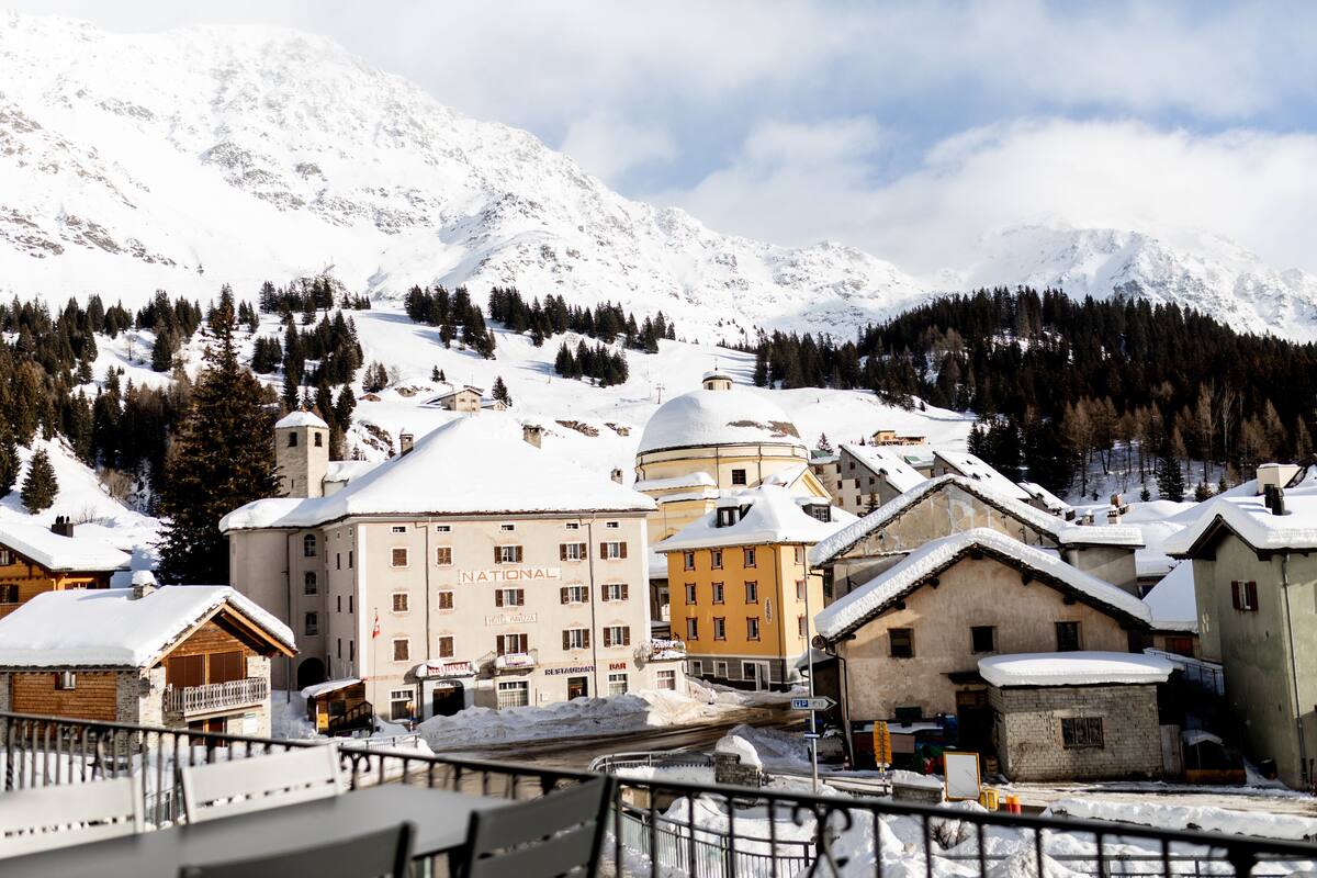A snow-covered mountain town with traditional buildings, including a prominent hotel with a dome and a sign that reads "NATIONAL".