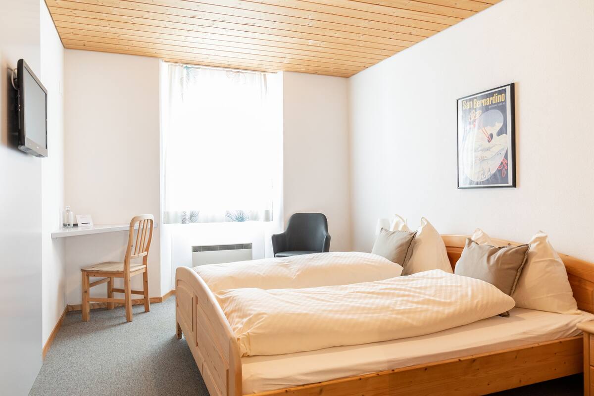 A hotel room with two single beds, a desk, a chair, a TV, and a poster on the wall.