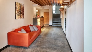 A modern interior with a stone floor, a wooden ceiling, a red sofa, and a staircase leading to an upper level.