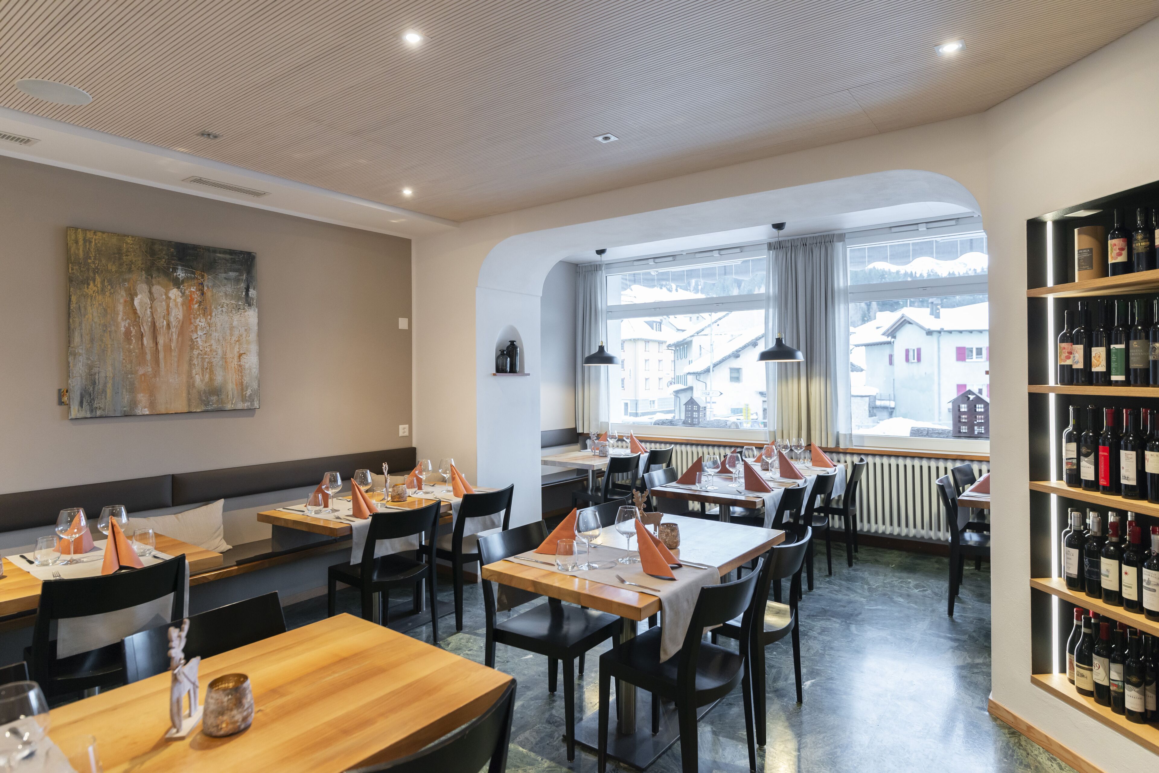 Ein Restaurant mit gedeckten Tischen, einer Weinstauraum und Blick auf Gebäude.