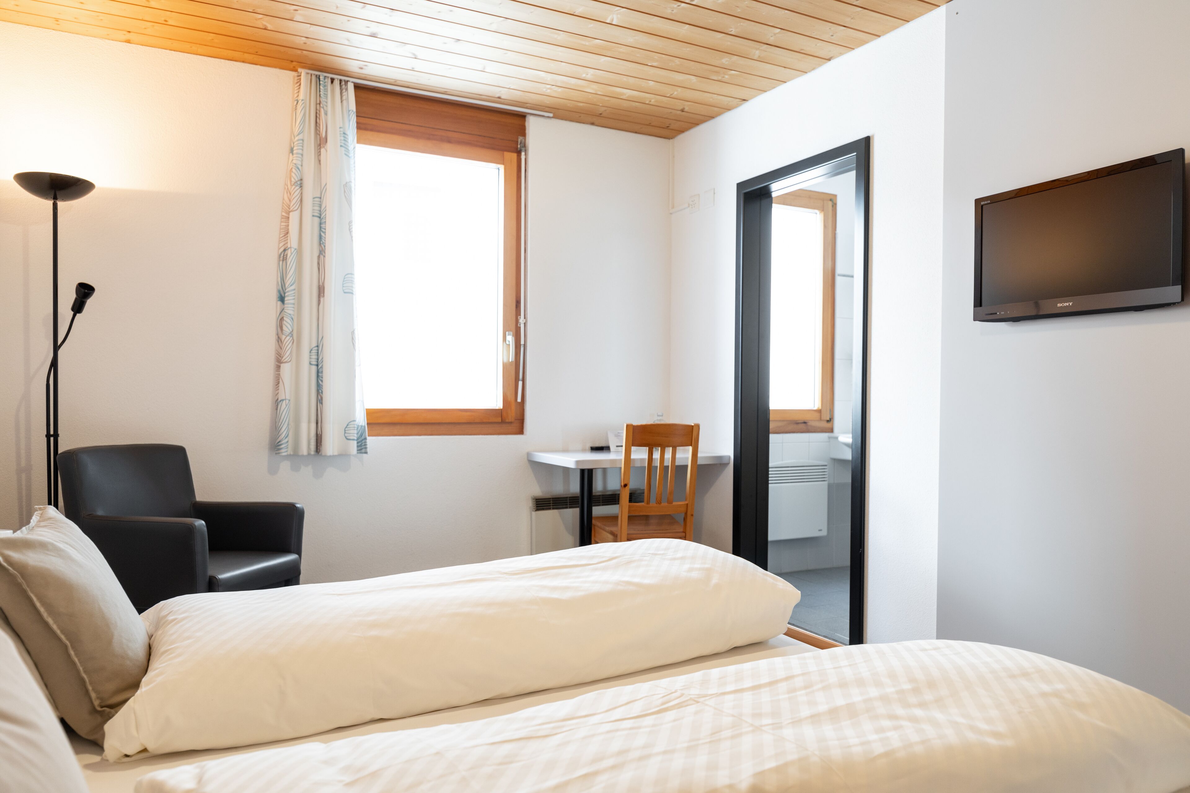 A bedroom with a bed, a desk, a chair, and a TV.
