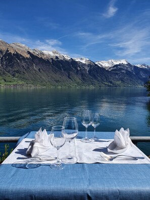 A table set with wine glasses and a napkin, overlooking a lake with mountains in the background. - Strandhotel (Iseltwald)