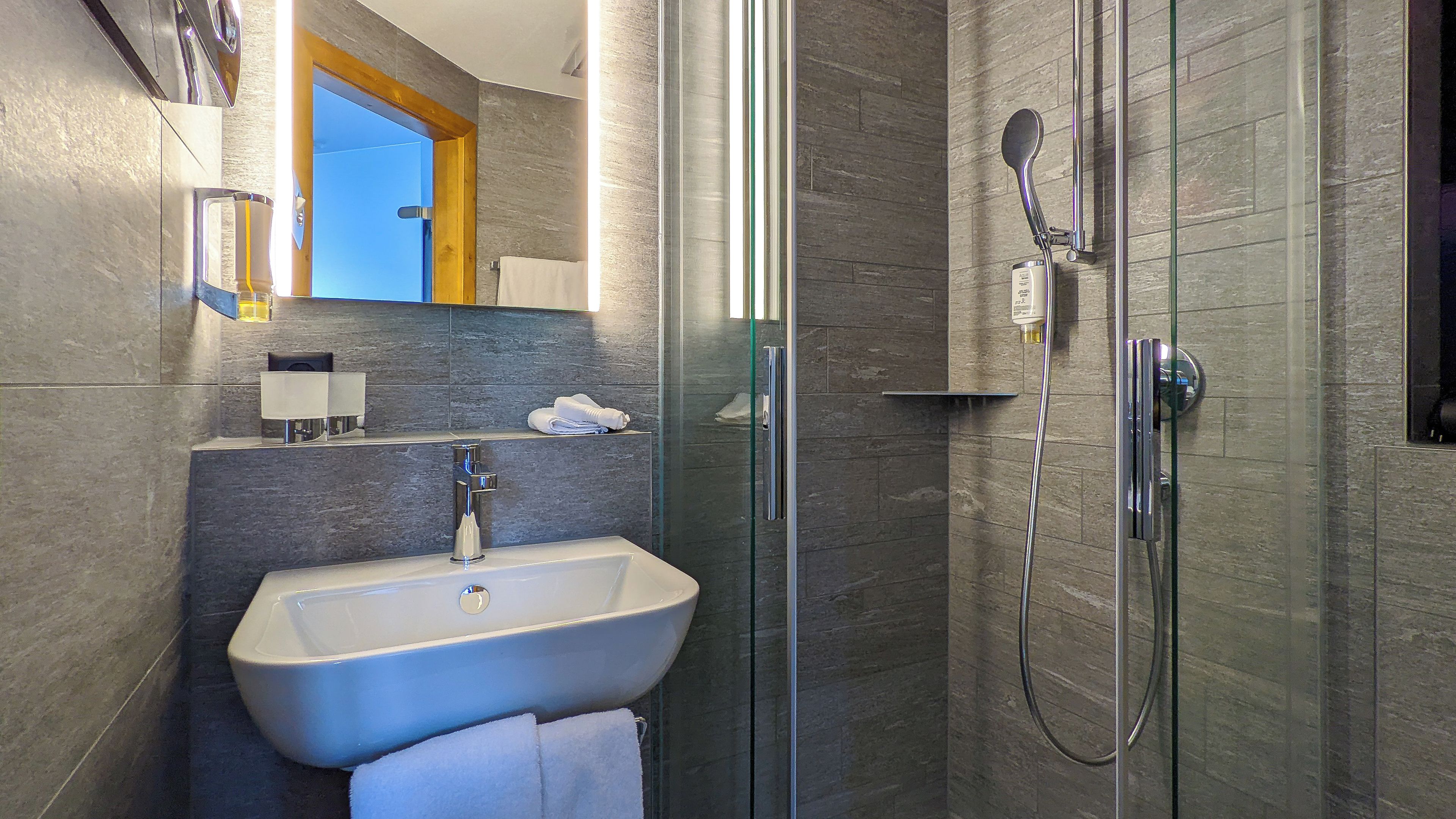 Un baño moderno con ducha envuelta en vidrio, lavamanos blanco y un espejo sobre él.