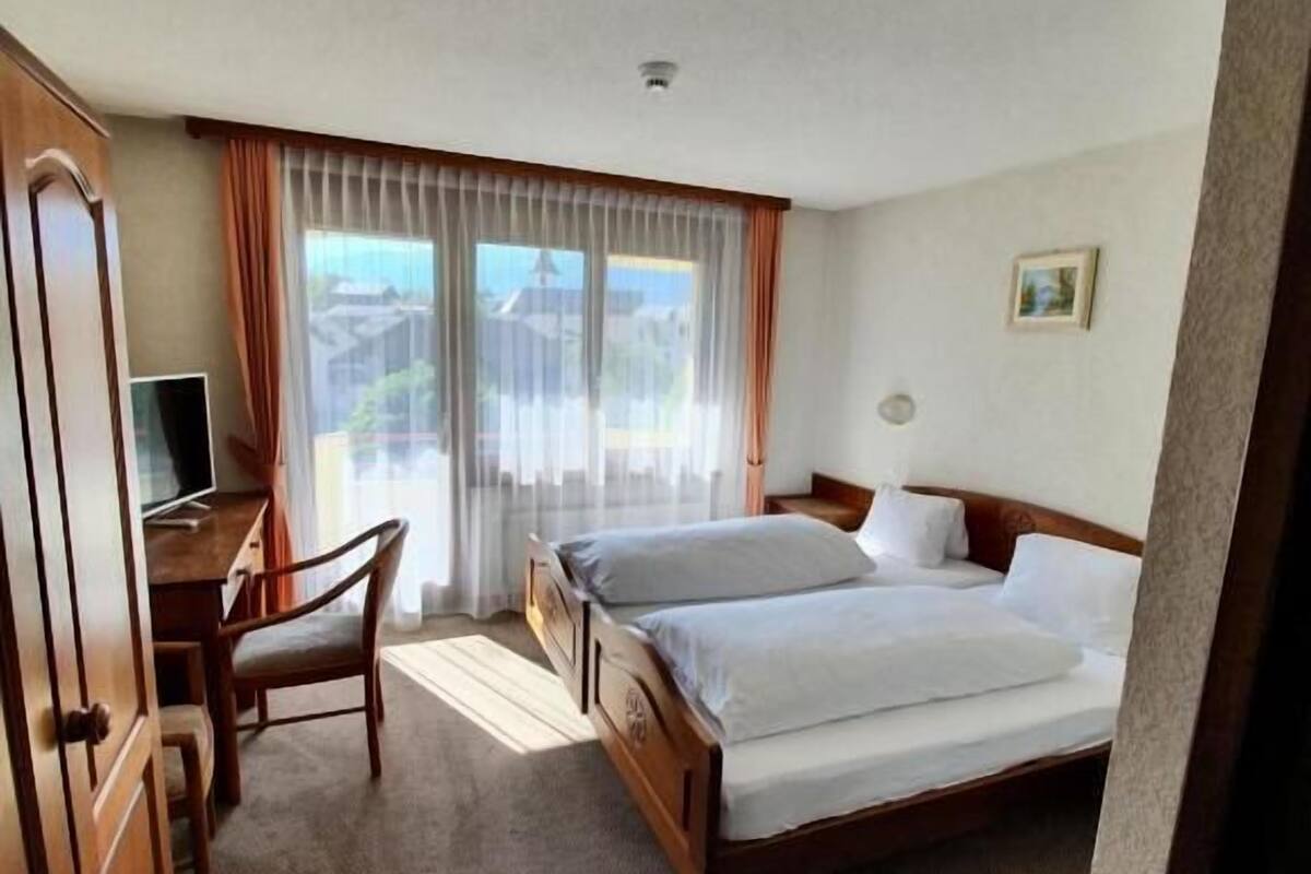 Een hotelkamer met een bed, een bureau, een stoel en een raam met gordijnen.