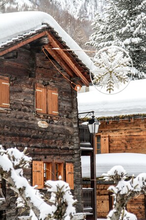 A rustic wooden building with snow-covered roof and windows, a sign indicating '6 rooms', and a street lamp. - Pointe de Zinal (Anniviers)
