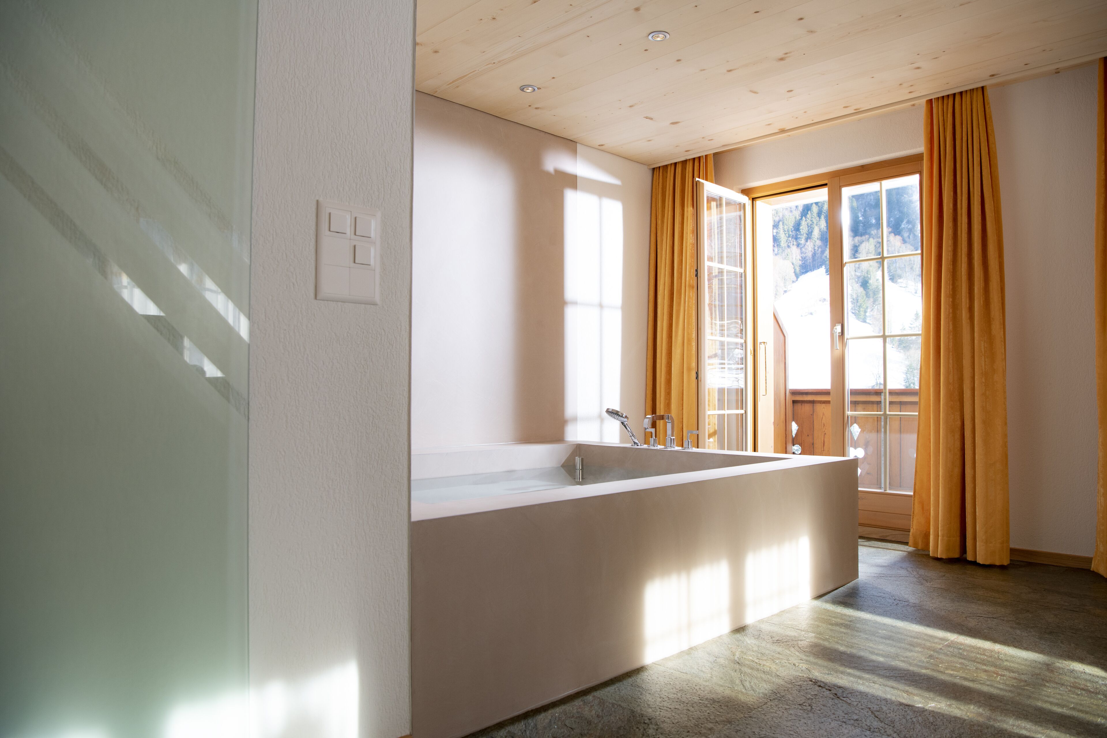 A modern bathroom with a large bathtub, a window with curtains, and a wooden ceiling.