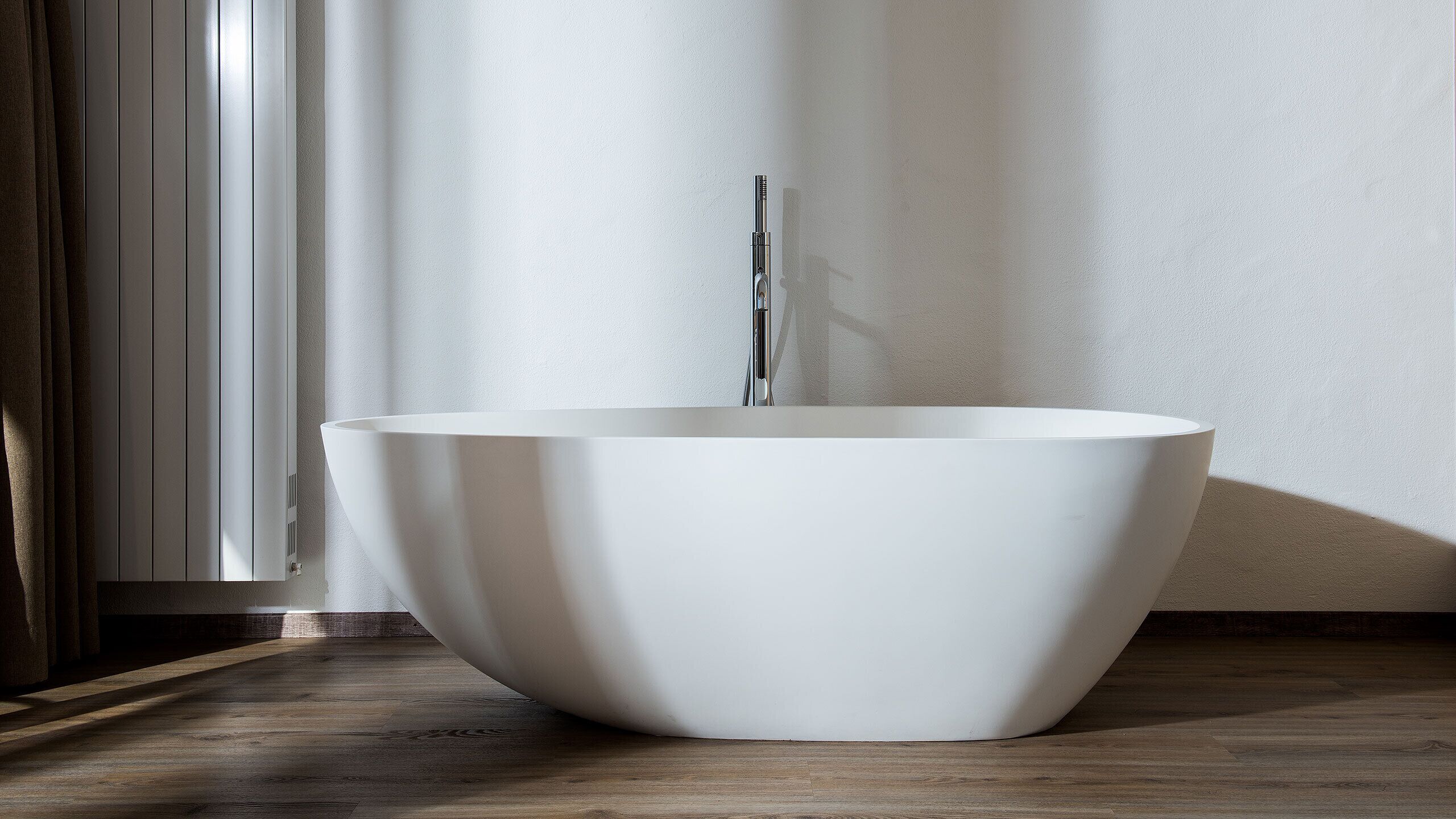 Una bañera blanca moderna, independiente, en un baño minimalista con suelo de madera y pared blanca.