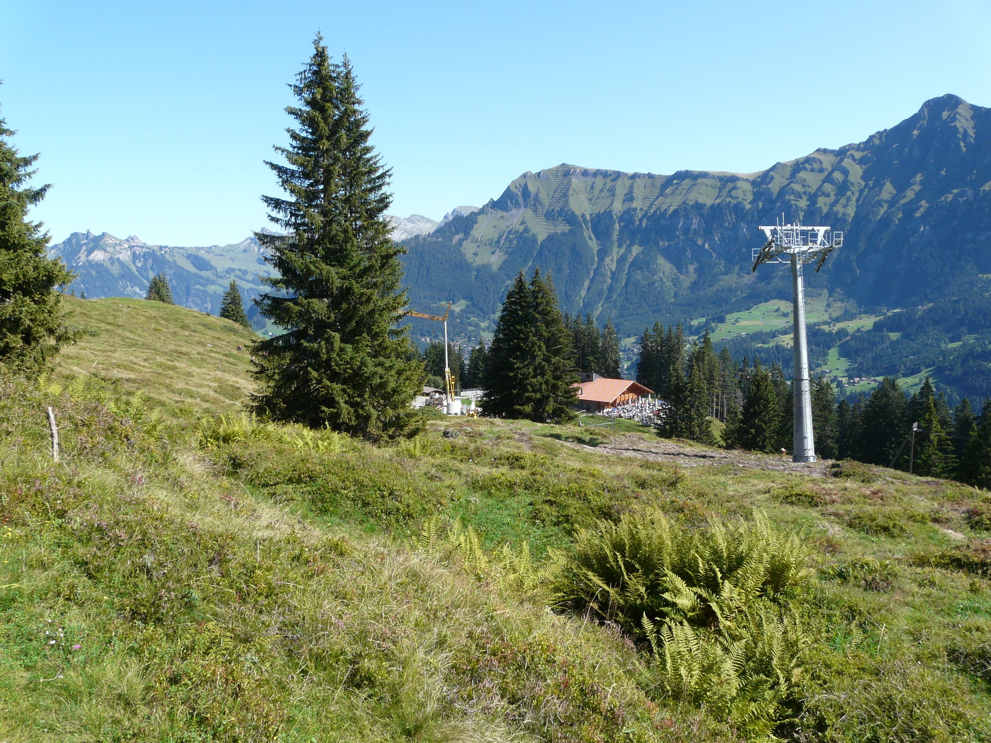 A mountain landscape with a ski lift, a building with a red roof, and a clear sky.