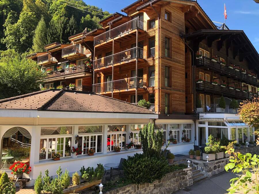 A multi-story wooden building with balconies, a covered outdoor seating area, and a mountain backdrop.