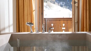 Un baño moderno con una bañera grande, marcos de ventana de madera y vistas a un paisaje nevado.