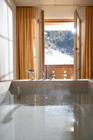 A modern bathroom with a large bathtub, wooden window frames, and a view of a snowy landscape.