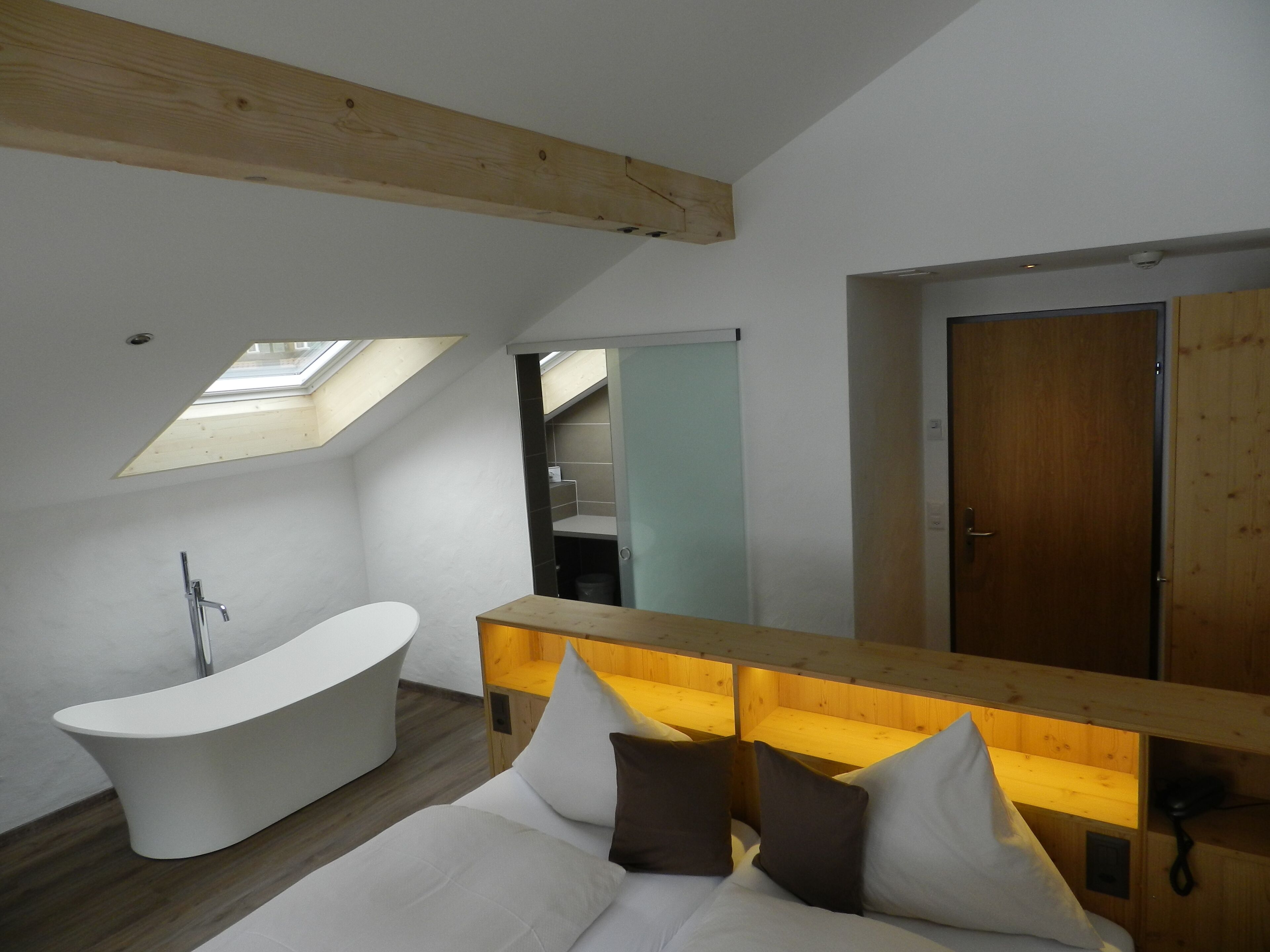 A modern bathroom with a freestanding bathtub, a wooden bench with cushions, and a skylight.