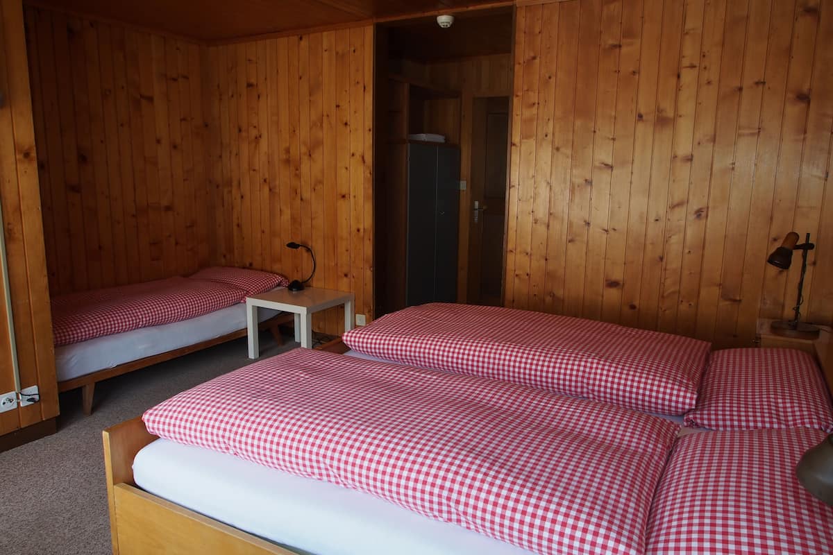 Uma cabana de madeira com duas camas de solteiro, uma mesa pequena e um guarda-roupa.