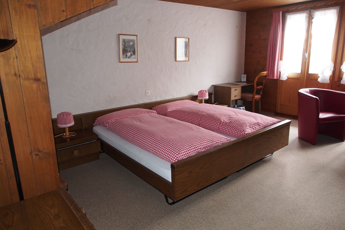 Um quarto com estrutura de madeira, uma cama, uma escrivaninha e uma cadeira.