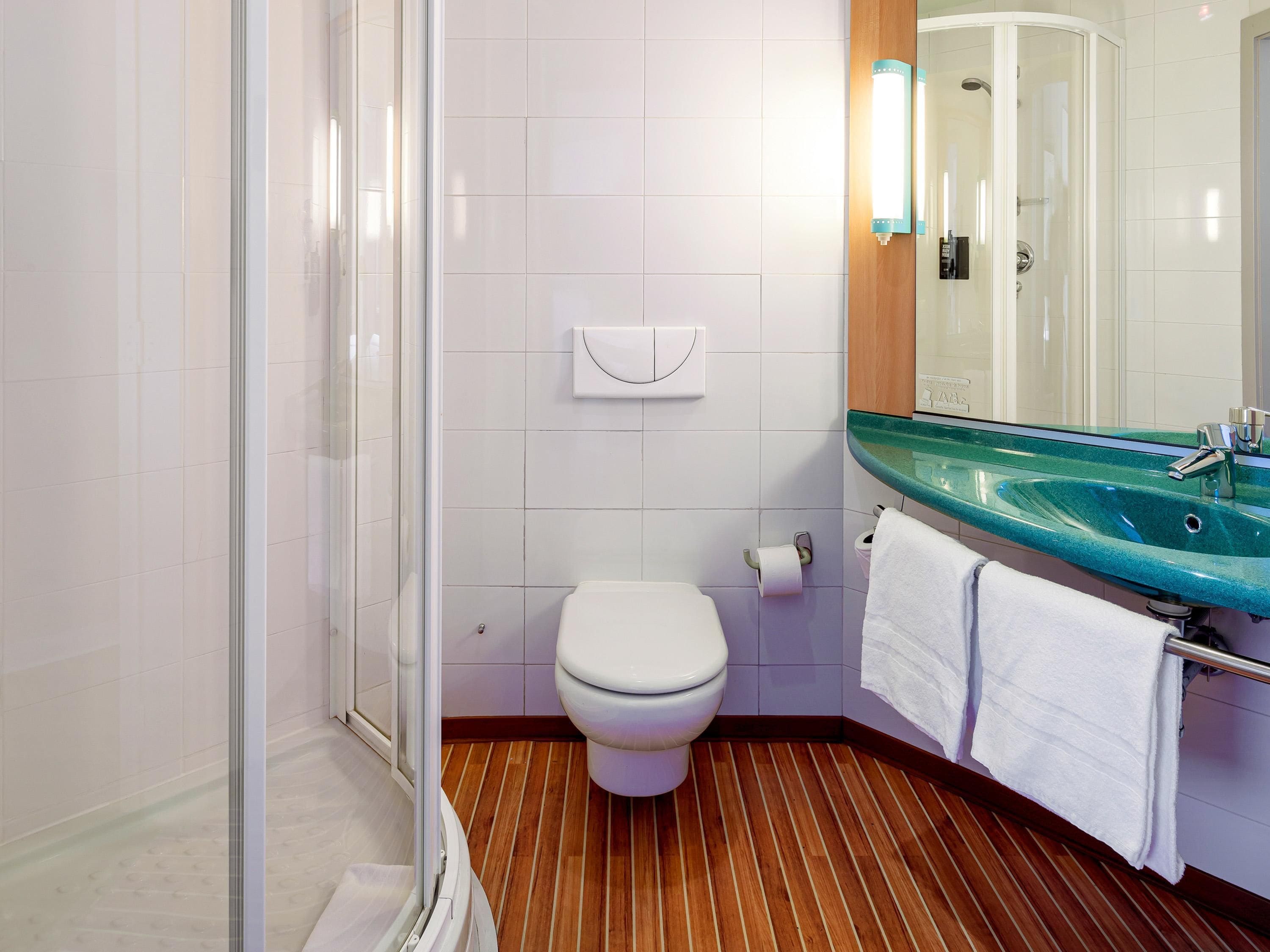 A bathroom with a glass sink, white toilet, and a shower enclosure.