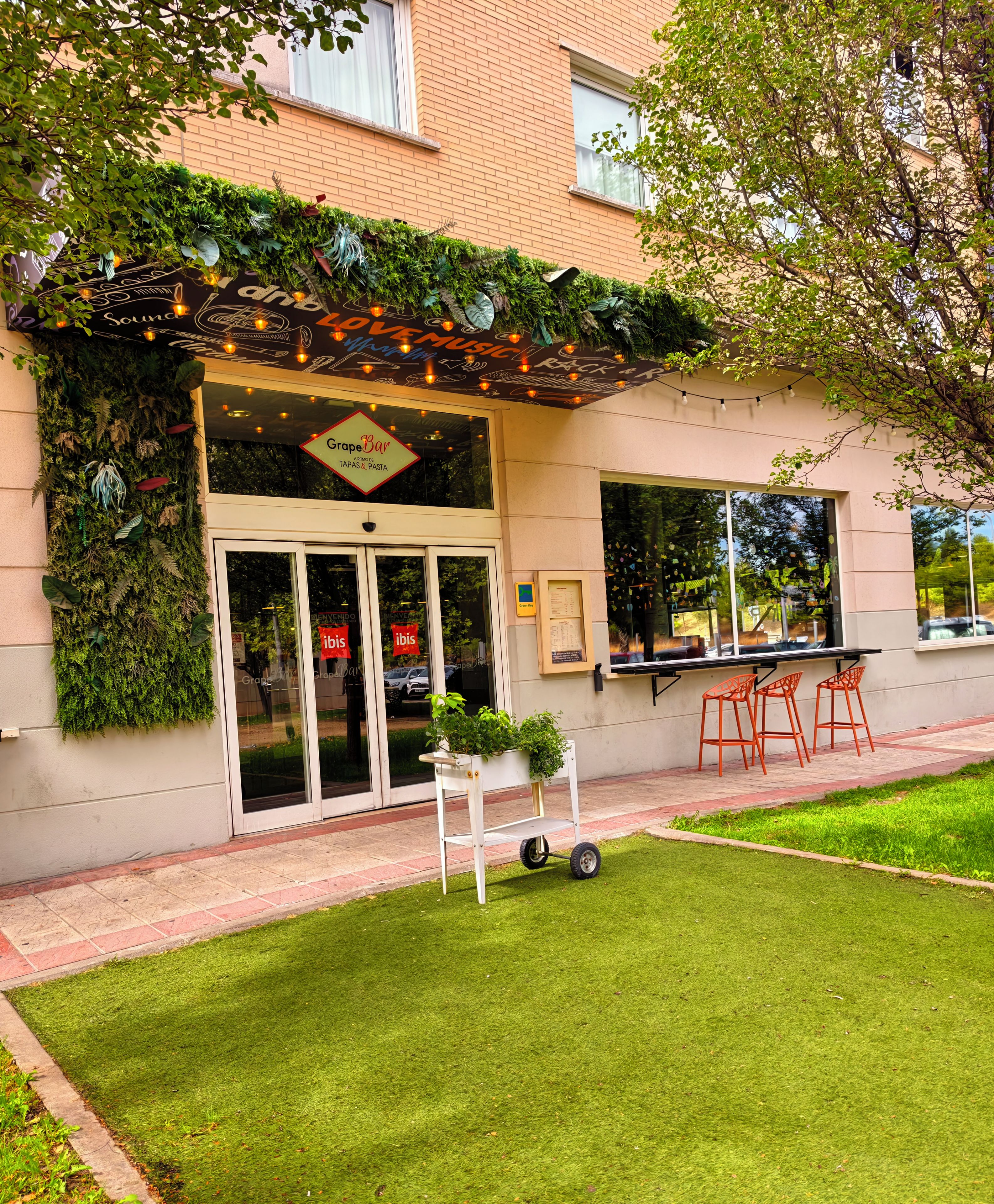 A restaurant with a green wall, outdoor seating, and a sign reading 'GrapeBar'.