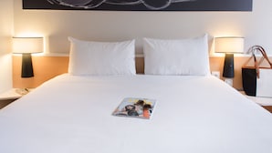 A neatly made bed with white linens, two bedside lamps, a magazine on the bed, and a large abstract painting on the wall. - Hotel ibis Madrid Getafe (Getafe)