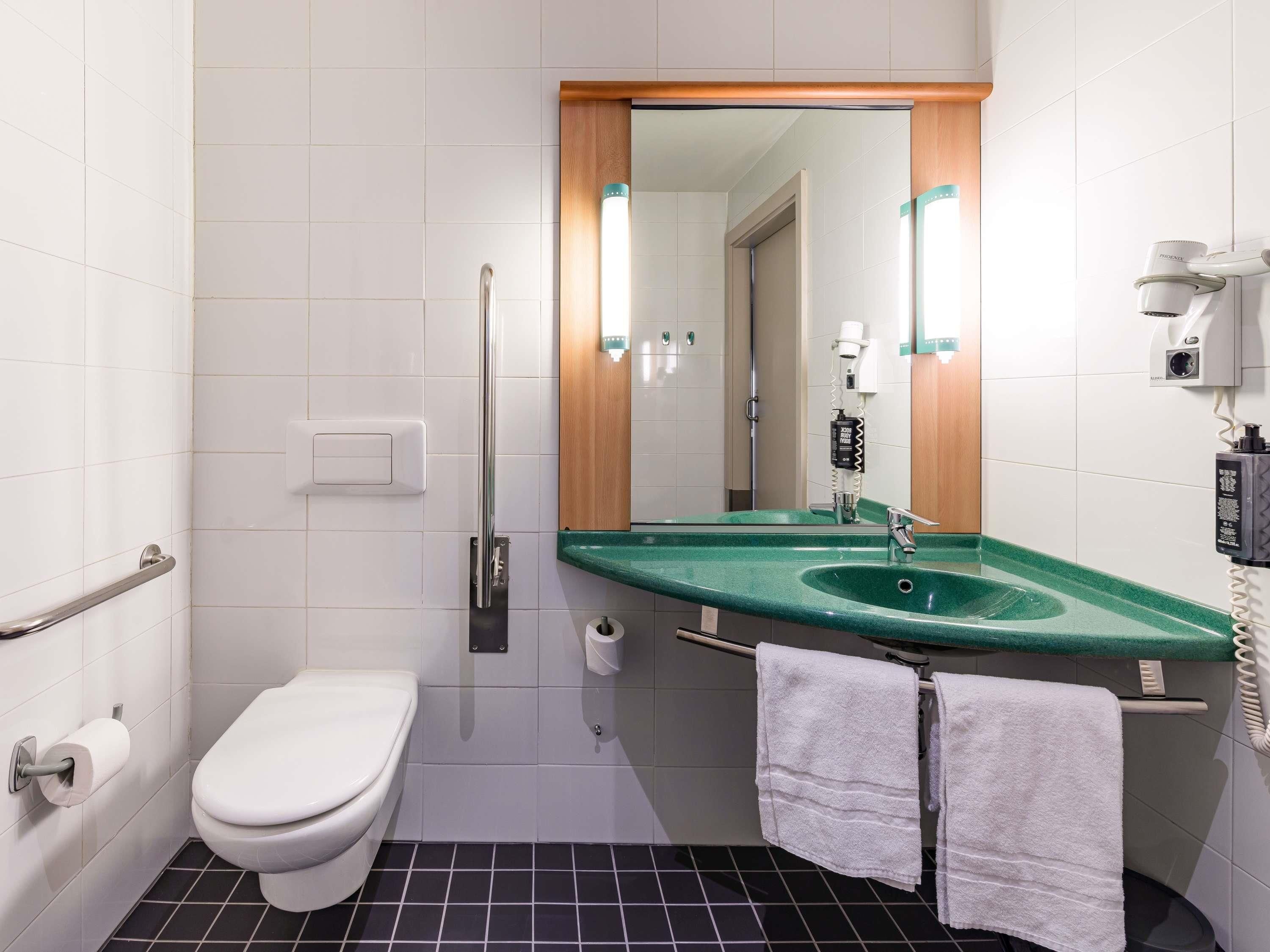 A bathroom with a toilet, a sink with a green countertop, a mirror, and a towel rack.
