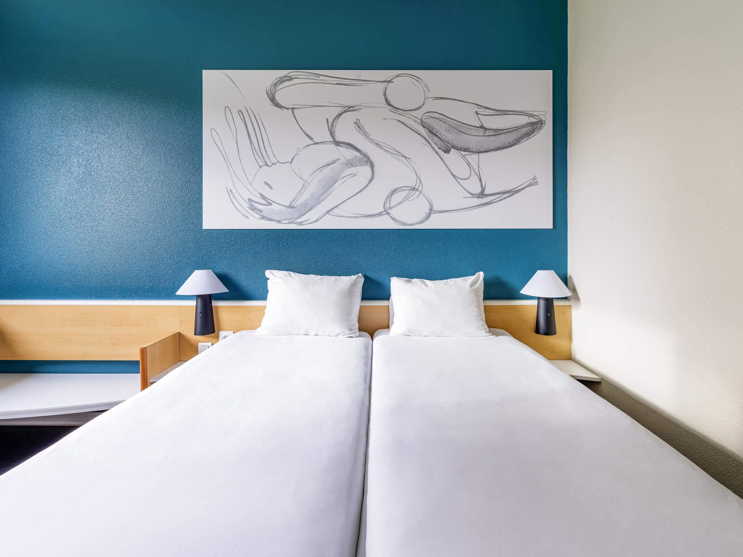 Une chambre d’hôtel avec un lit, deux lampes de chevet, une œuvre d’art murale et un mur d’accent bleu.