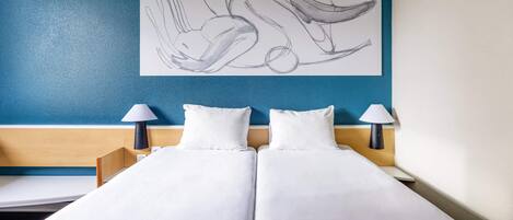 Une chambre d’hôtel avec un lit, deux lampes de chevet, une œuvre d’art murale et un mur d’accent bleu.