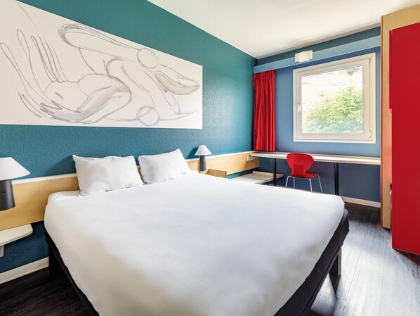 A hotel room with a large bed, a desk, a chair, a window with red curtains, and a wall art piece. - Hotel ibis Madrid Getafe (Getafe)
