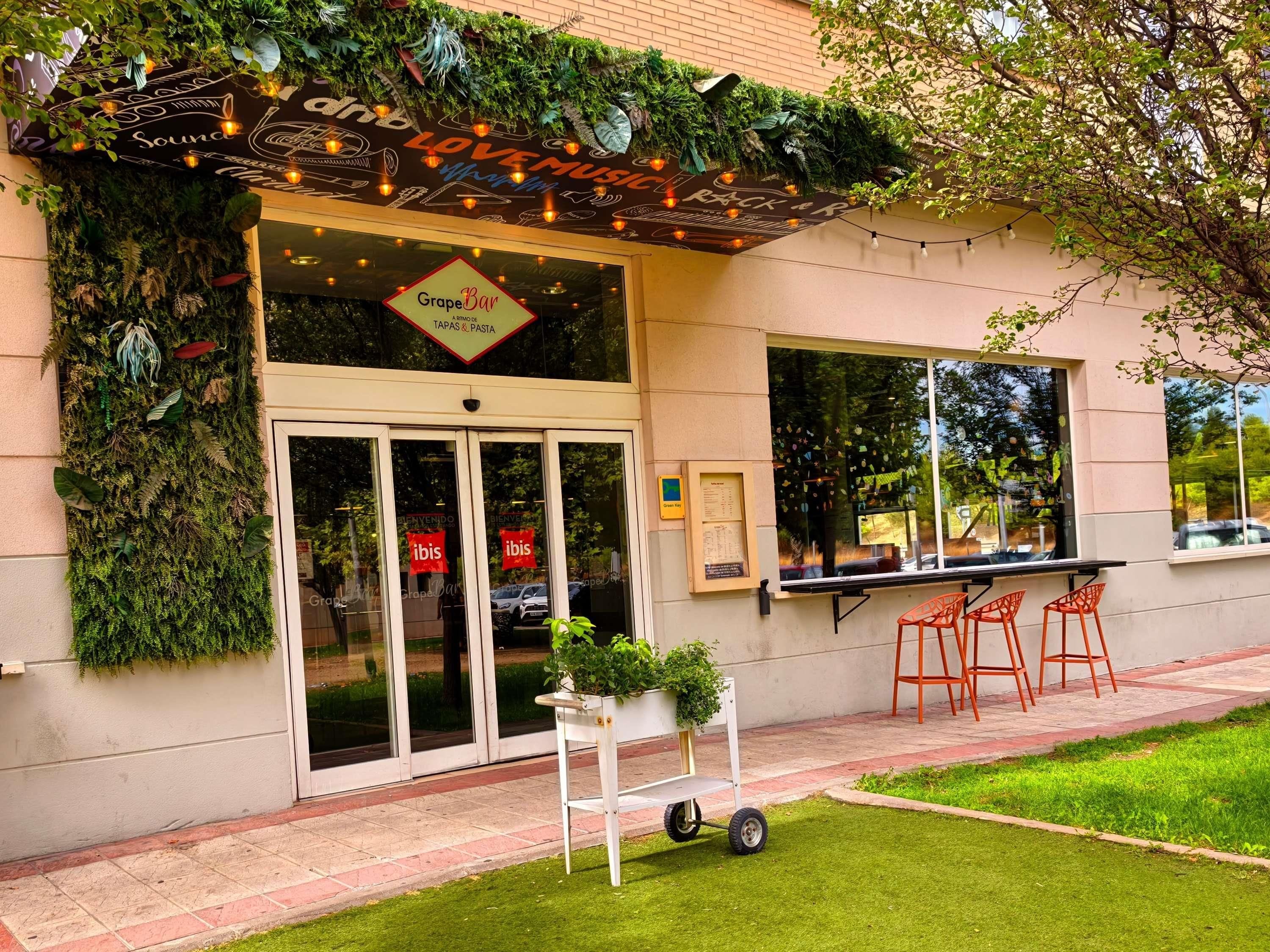 Un restaurante con un letrero que dice 'GrapeBar TAPAS & PASTA' y una pared verde con plantas.