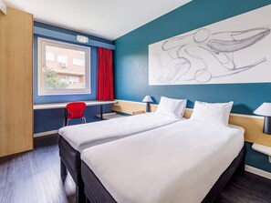 A hotel room with a bed, a desk, a chair, a window, and a wall art piece. - Hotel ibis Madrid Getafe (Getafe)