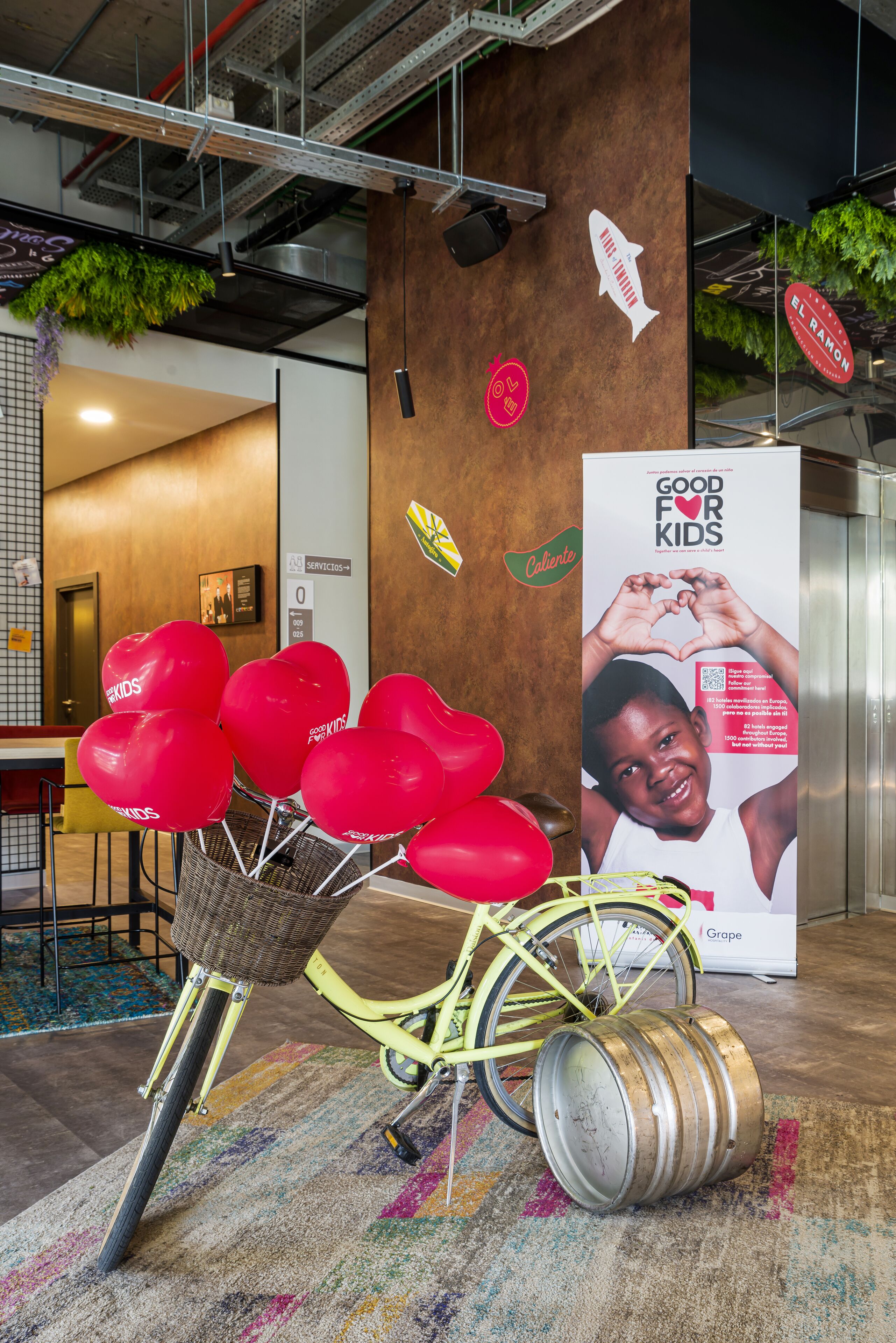 Un vélo avec un panier rempli de ballons rouges, une affiche représentant un enfant faisant un cœur avec ses mains, et un panneau orné d’un symbole de poisson.