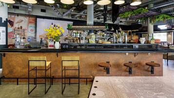 A bar area with a counter, bar stools, hanging pendant lights, and a variety of bottles and glasses.
