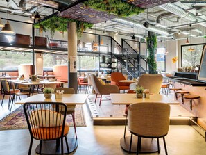 Ein modernes Café mit Zimmerpflanzen, einer Treppe und verschiedenen Sitzmöglichkeiten.