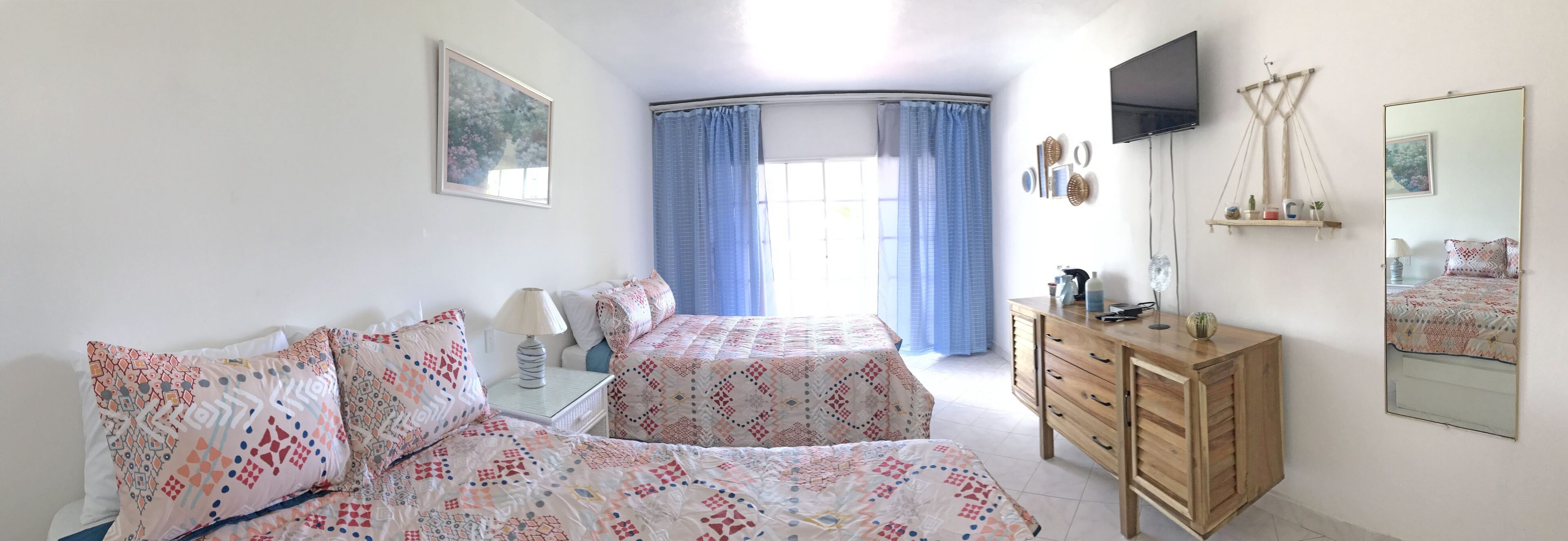 A bedroom with two beds, a wooden dresser, a TV, and a window with curtains.