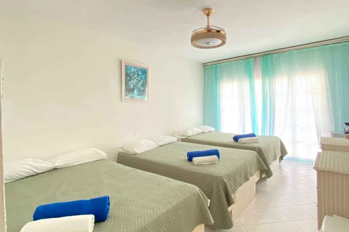Ein Hotelzimmer mit zwei Einzelbetten, einem Deckenventilator, einem kleinen Schreibtisch und einem Fenster mit Vorhängen.
