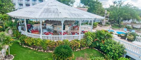 A gazebo with a thatched roof, surrounded by a white picket fence, and a pool in the background.