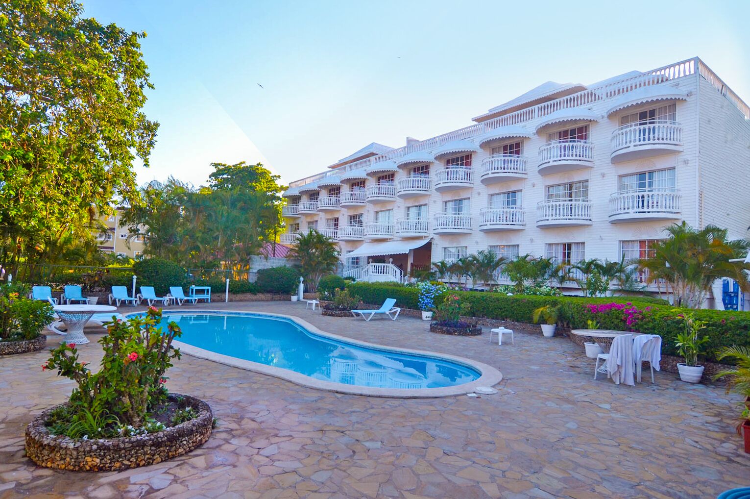 Un hotel con piscina rodeada de sillas de descanso y plantas en macetas.
