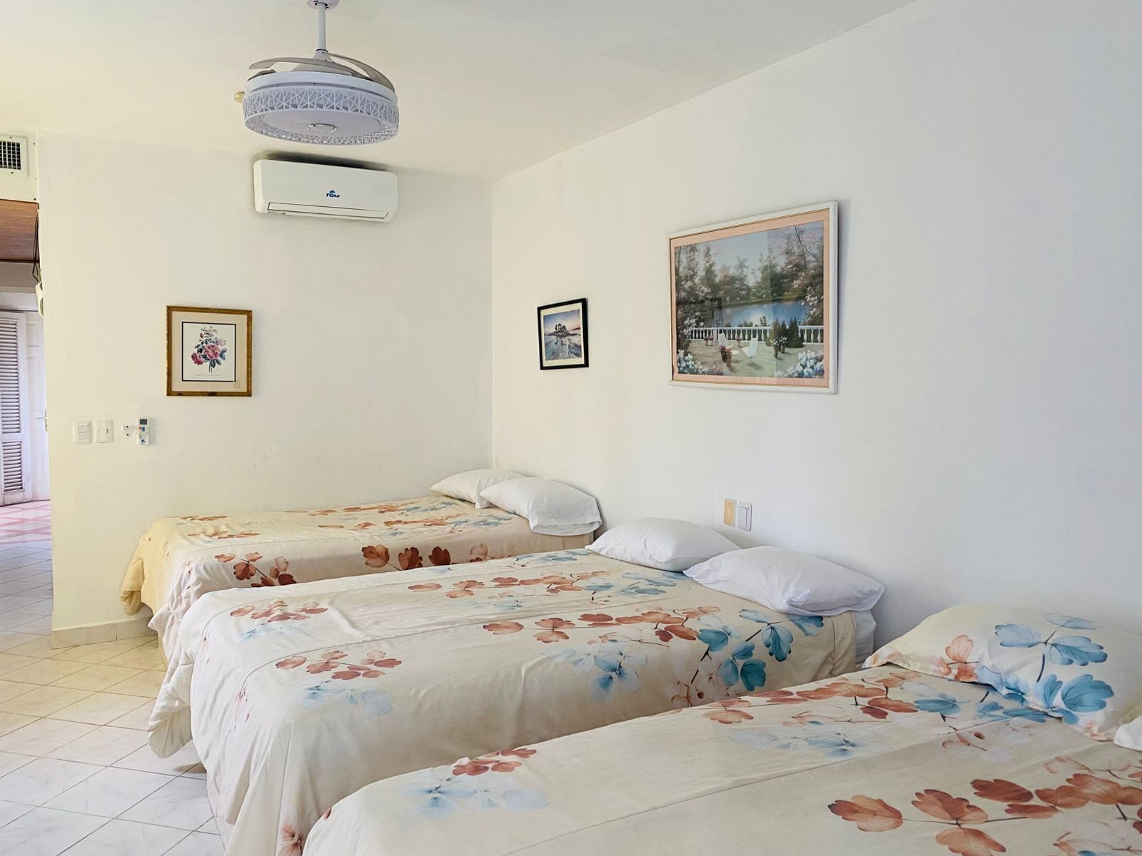 Ein Schlafzimmer mit zwei Betten, einem Deckenventilator, einer Klimaanlage und zwei gerahmten Bildern an der Wand.