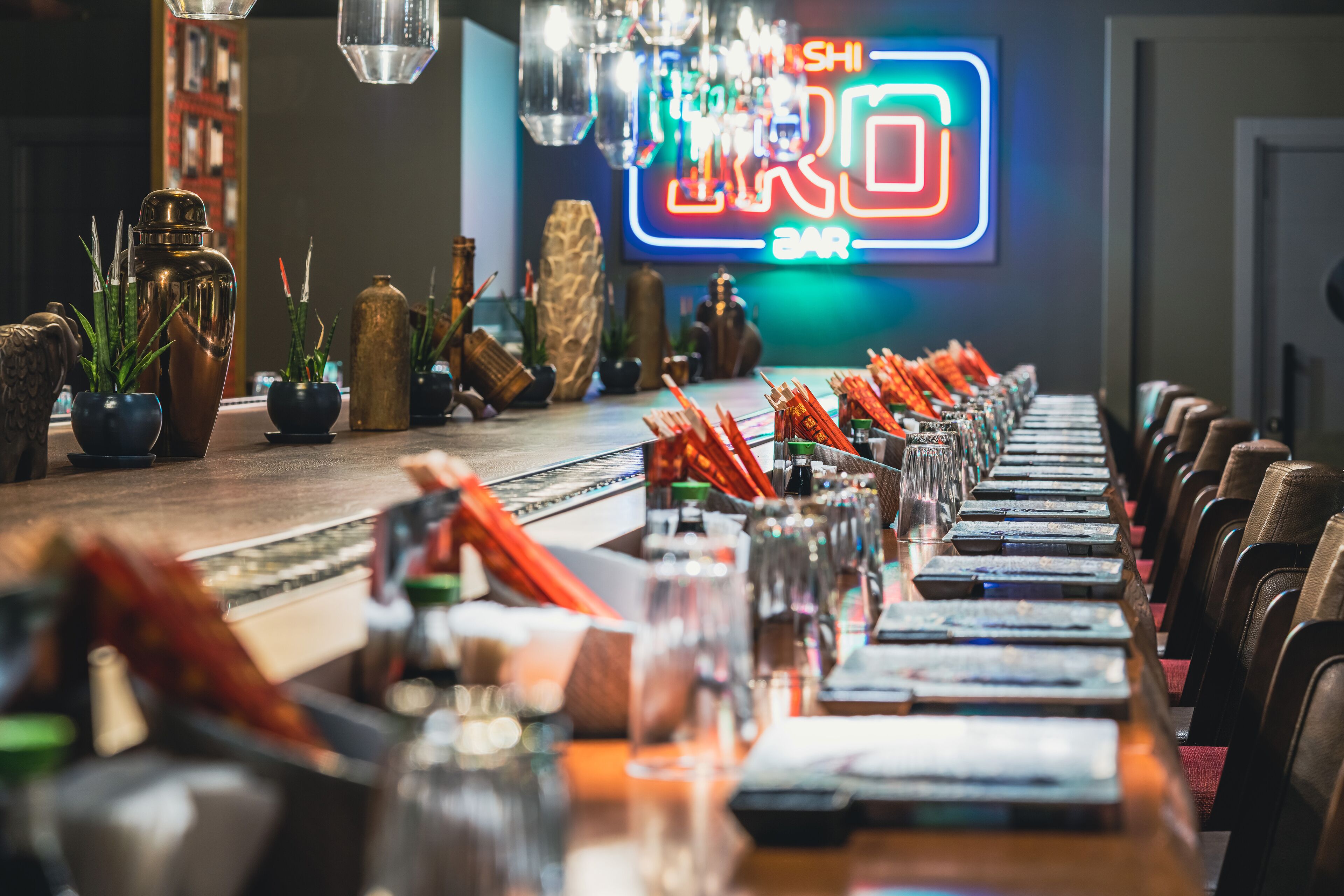 A bar with a neon sign, bottles, glasses, and a long counter.