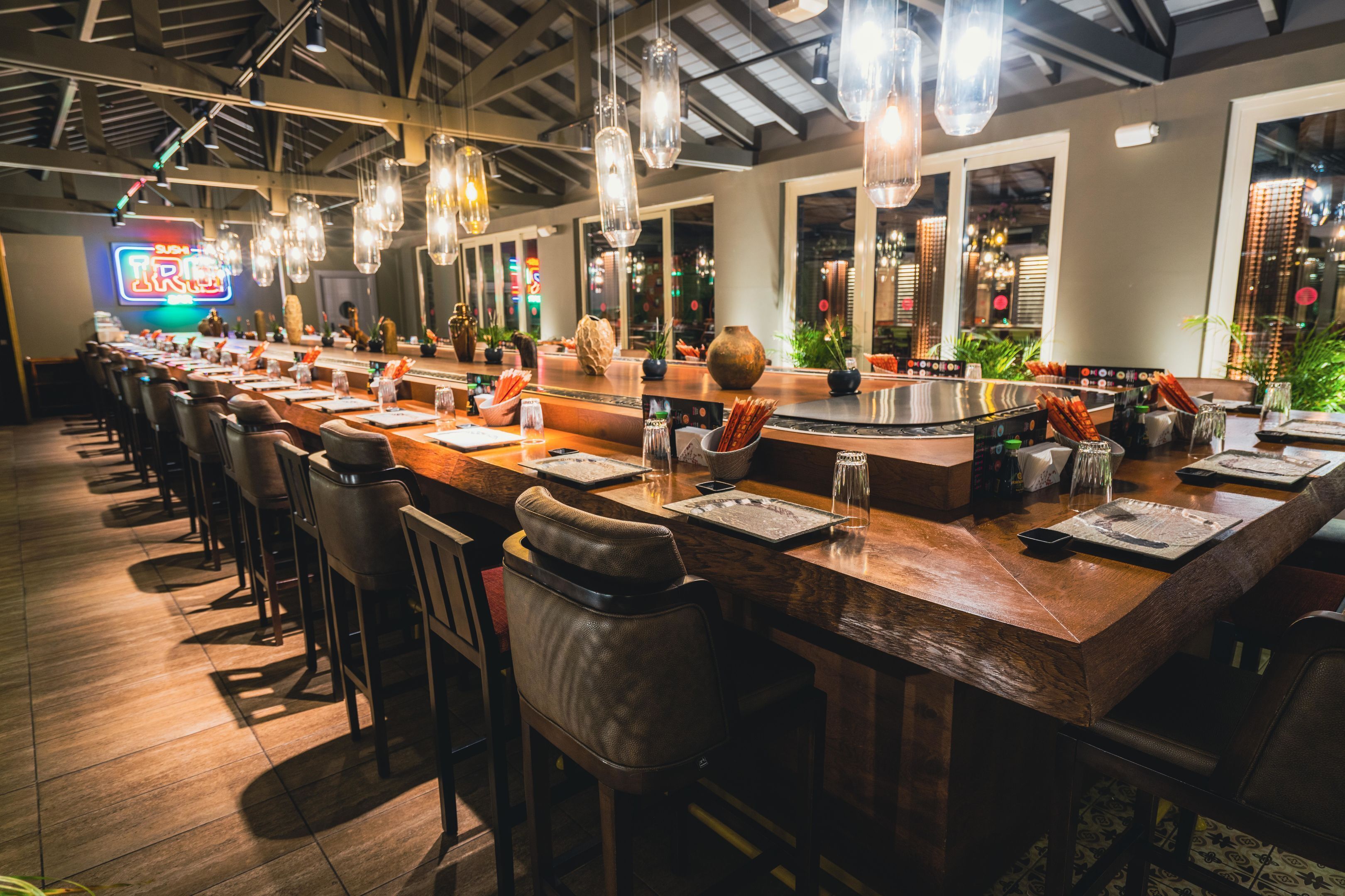 Uma área de bar com vários arranjos de assentos, um balcão comprido e luminárias pendentes.