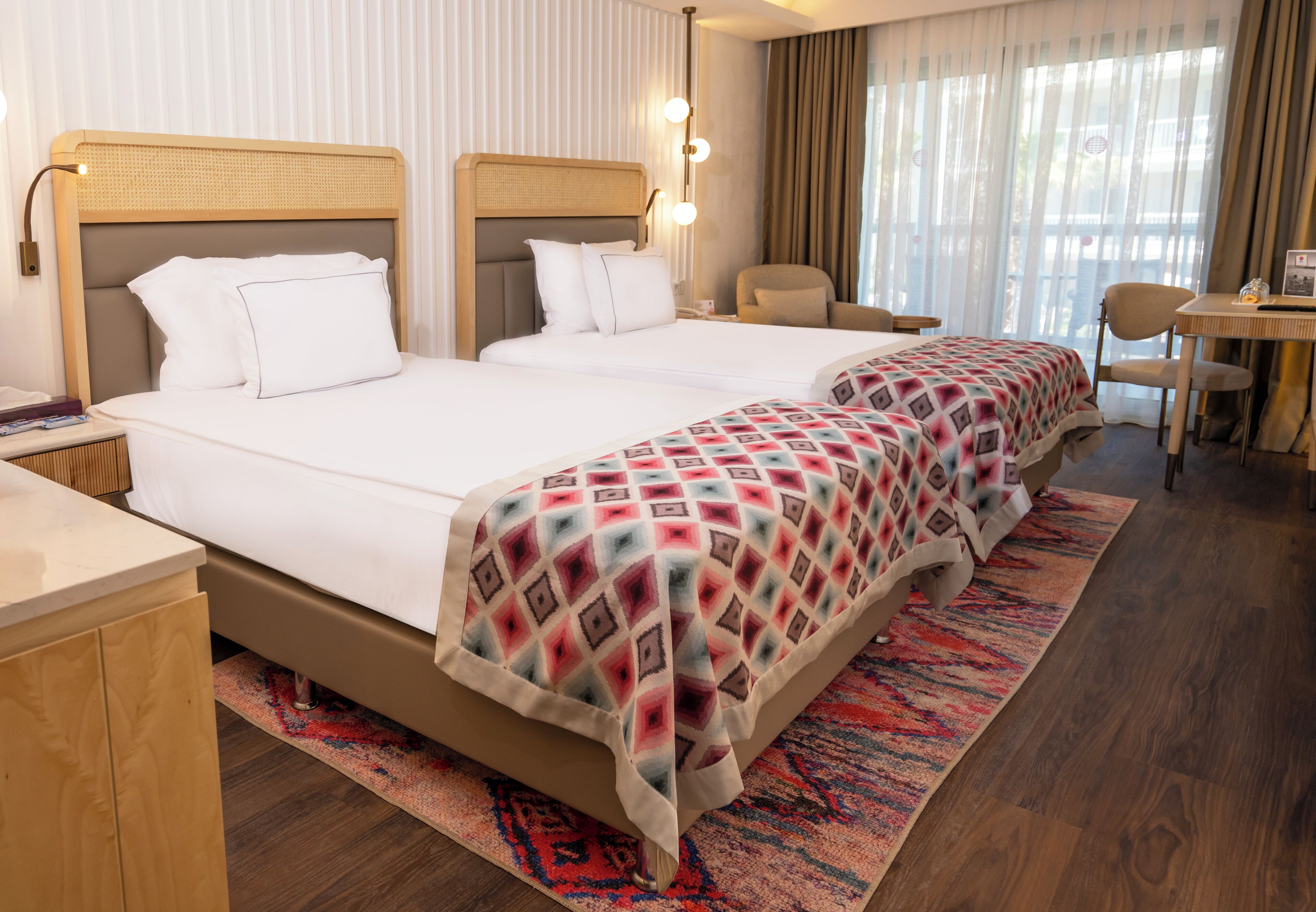 A hotel room with two beds, a desk, a chair, and a window with curtains.