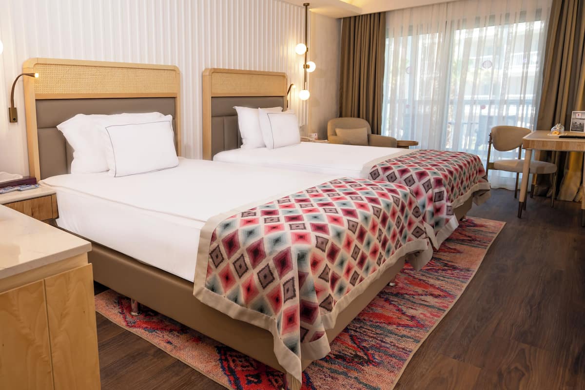 A hotel room with two beds, a desk, a chair, and a window with curtains.