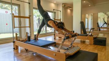Un estudio de Pilates con suelos de madera, máquinas de Pilates reformer y grandes ventanales con vistas a palmeras.