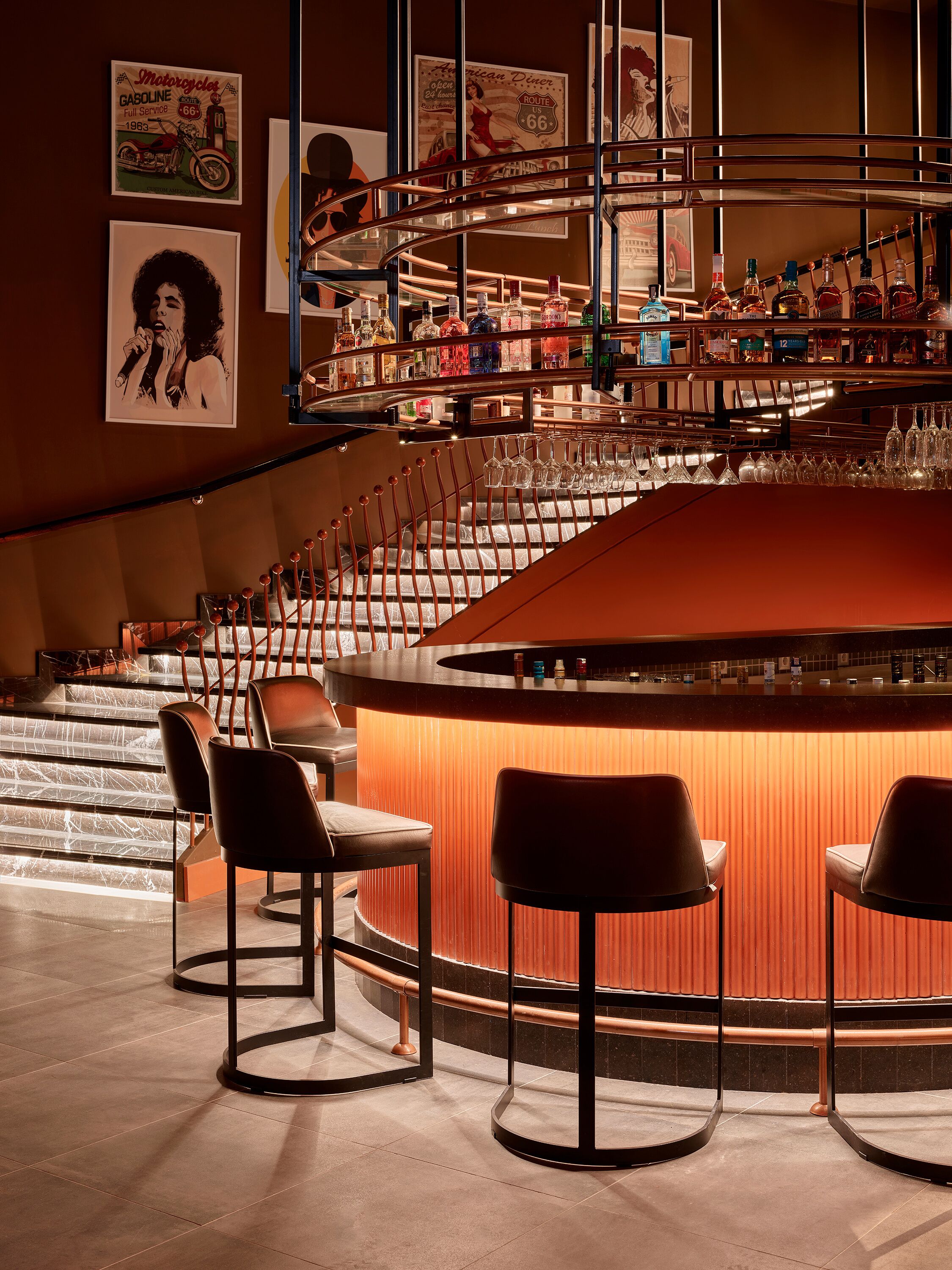Zona de bar con una barra curva, taburetes y una escalera que sube a un nivel superior.