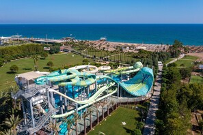 A water park with multiple slides and pools, surrounded by greenery and a view of the sea.