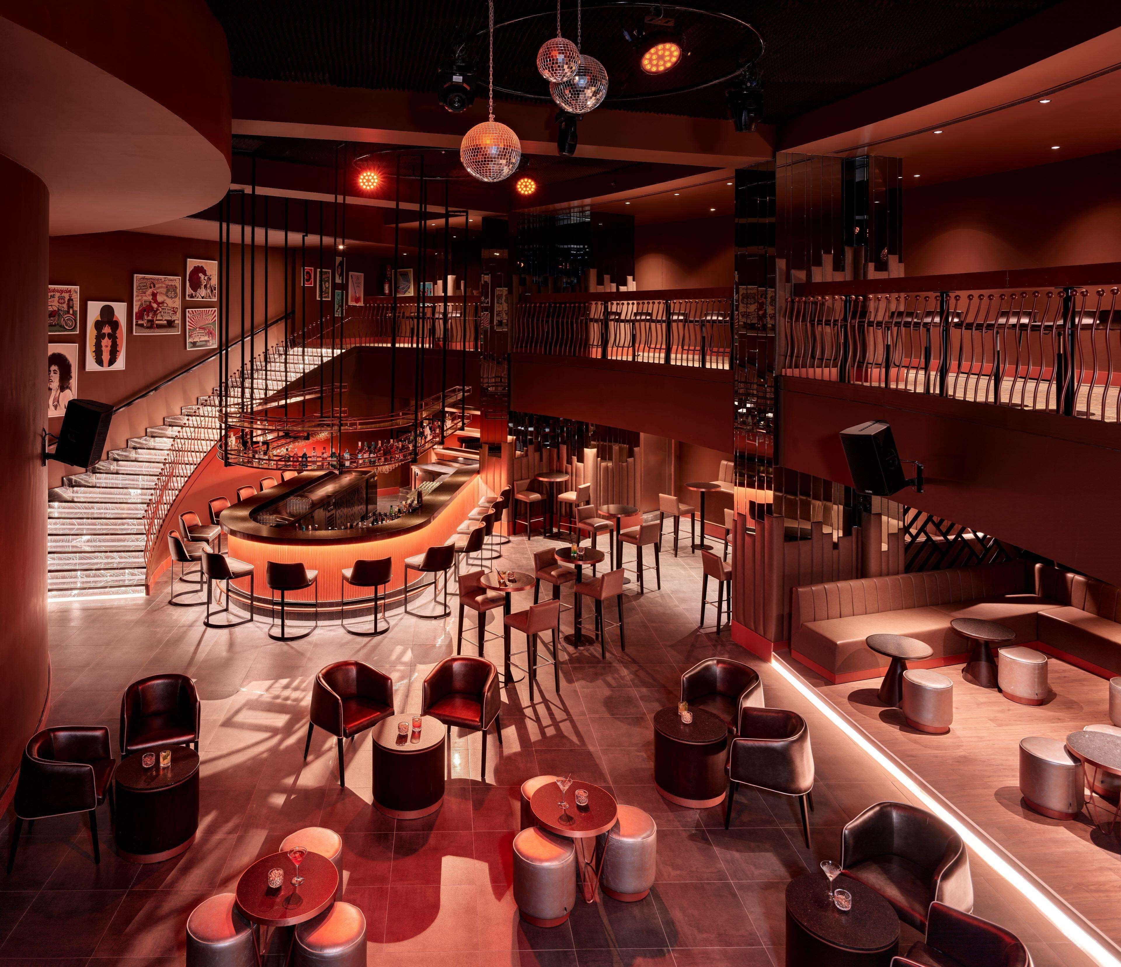 A modern bar area with a circular bar, multiple seating options, and a staircase leading to an upper level.