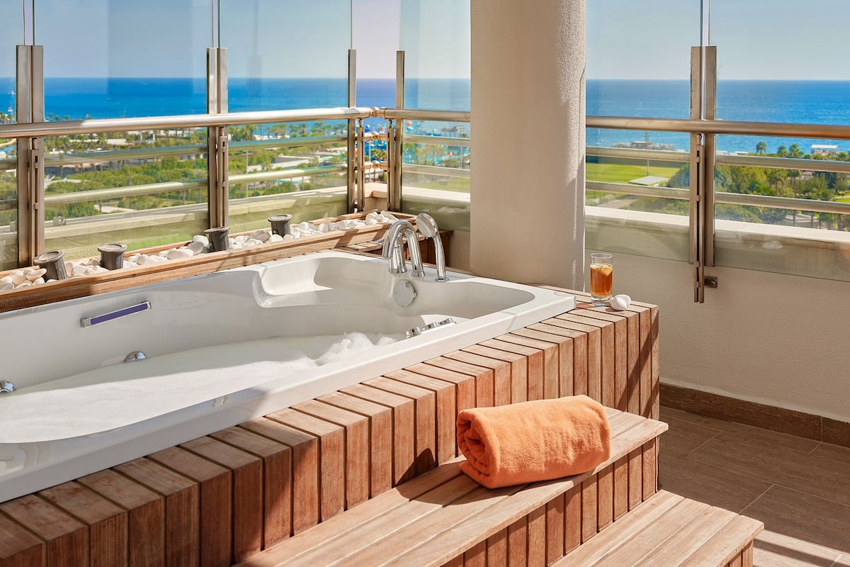 A modern bathroom with a large bathtub, wooden steps, and a view of the ocean.