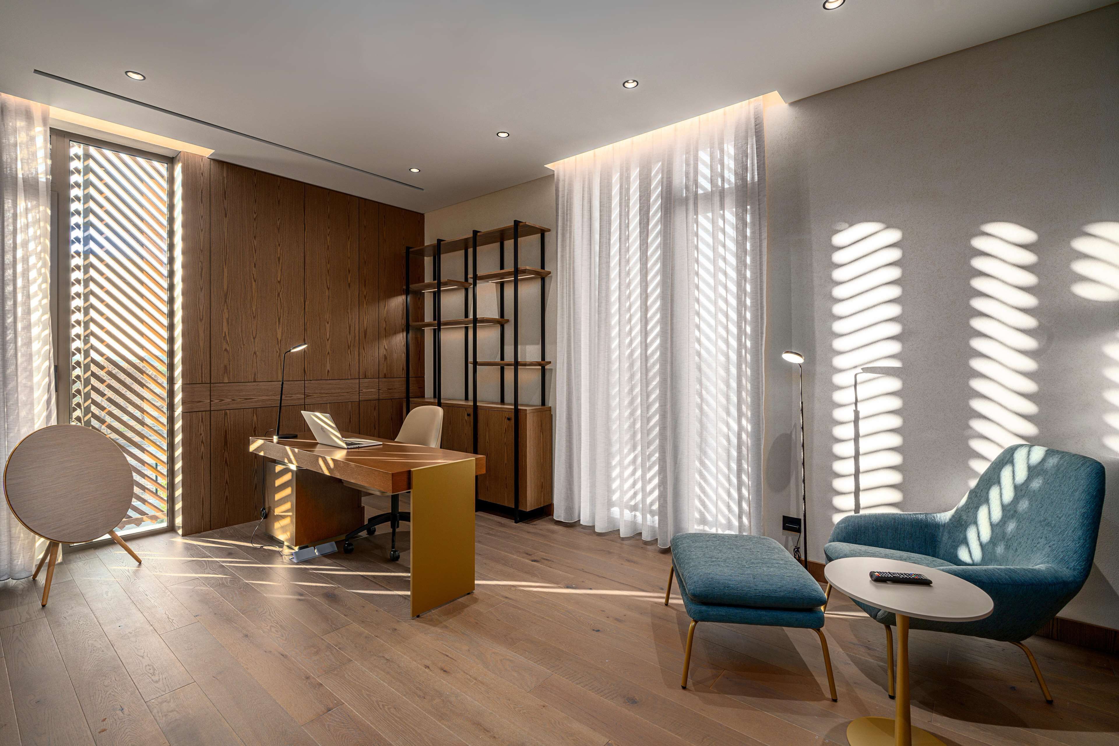 A modern room with a wooden desk, a blue armchair, and a round table with a remote control.