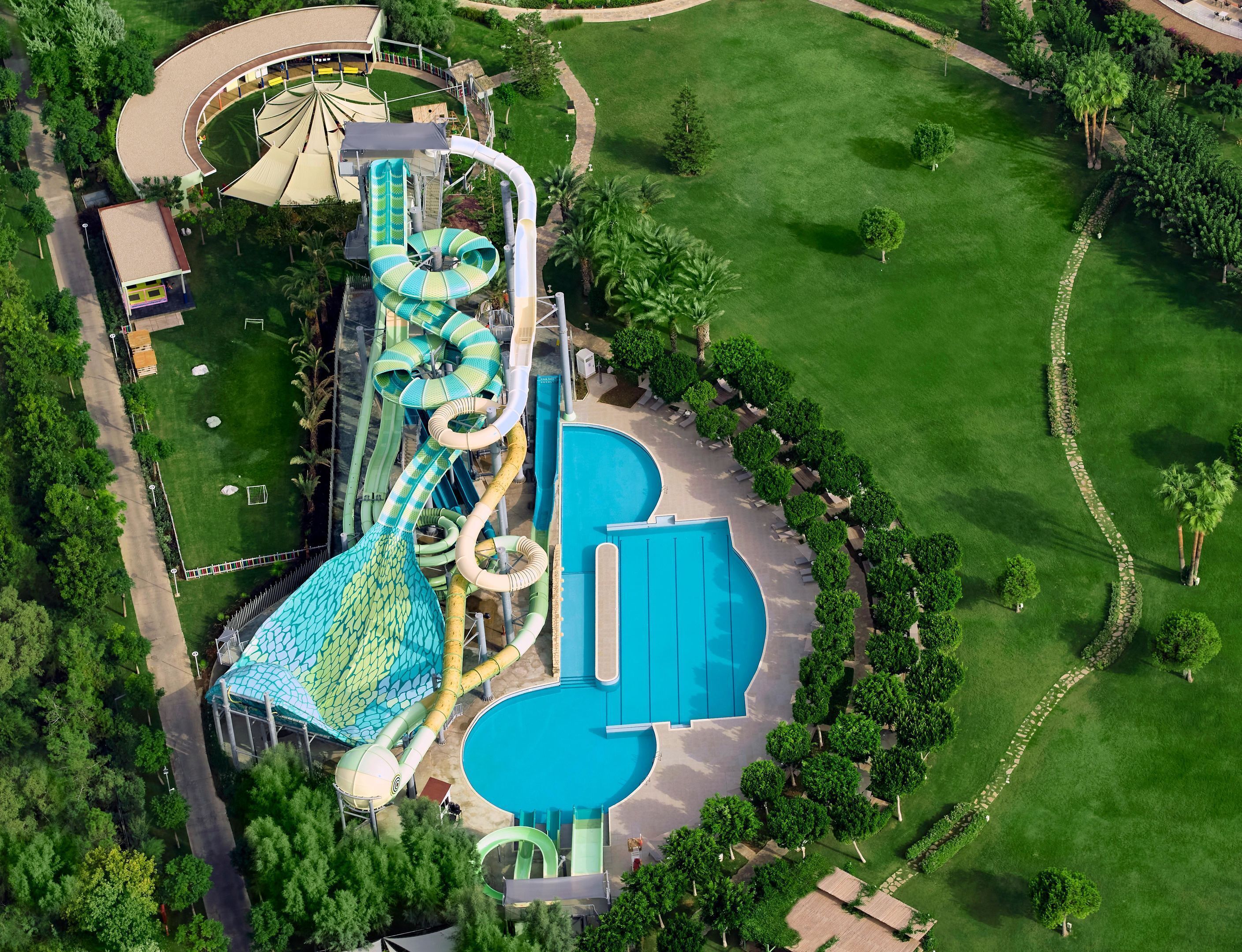 Luftaufnahme eines Wasserparks mit großem Pool, mehreren Rutschen und umgebender Bepflanzung.