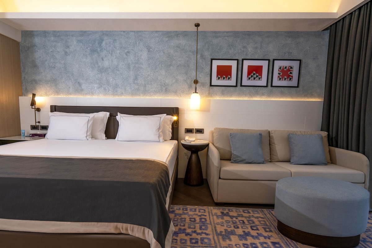 A hotel room with a large bed, a sofa, a small table, and a patterned rug.