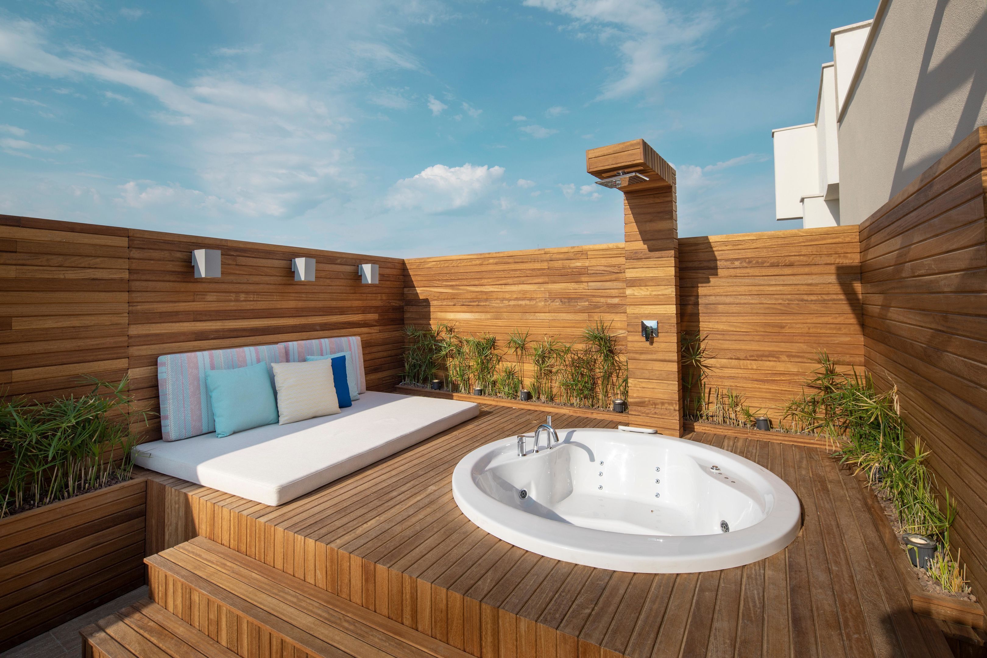 A wooden deck with a hot tub, a sofa with cushions, and potted plants.