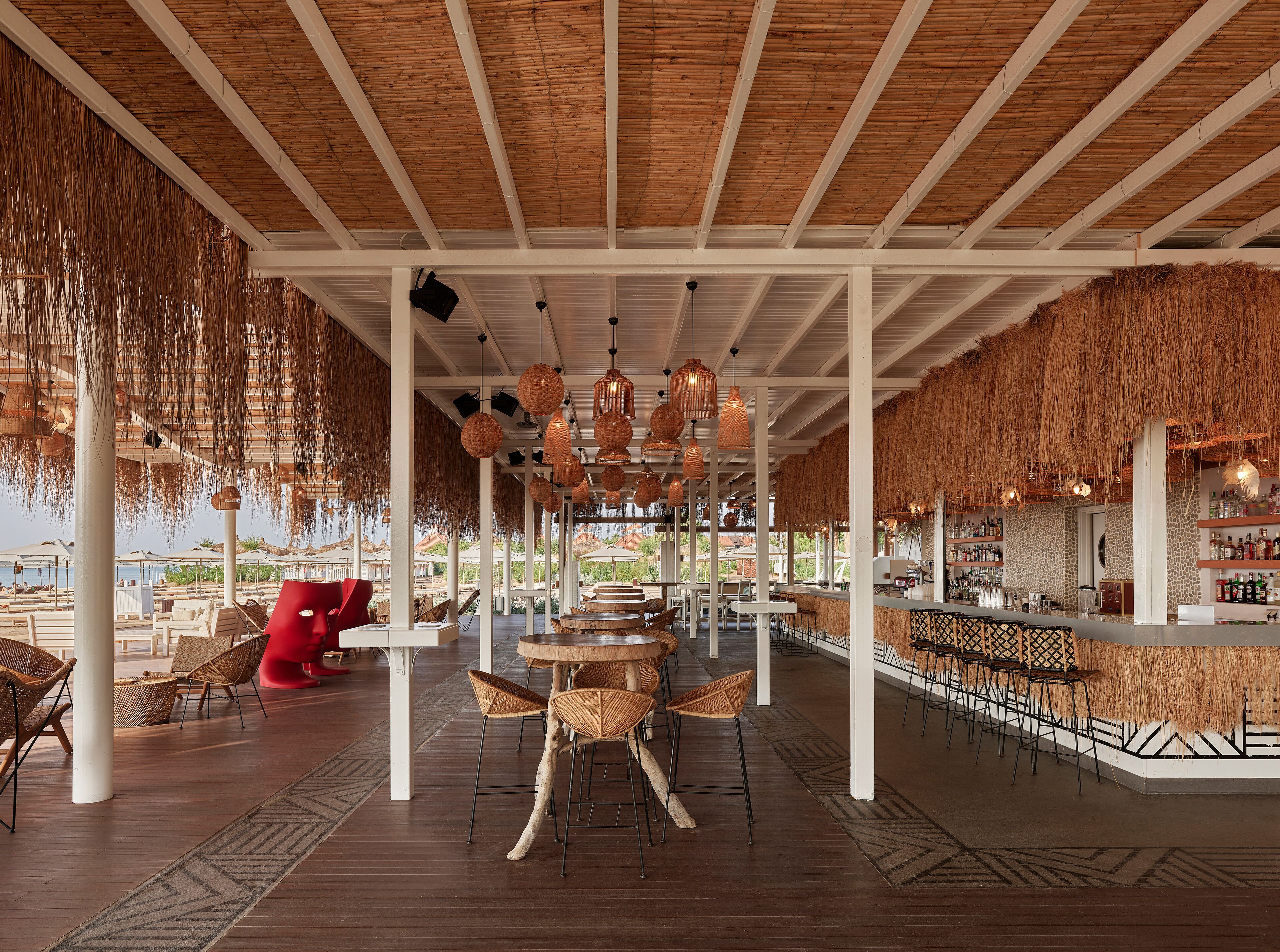 A spacious indoor area with high ceilings, hanging wicker lamps, and a bar area with stools and shelves.