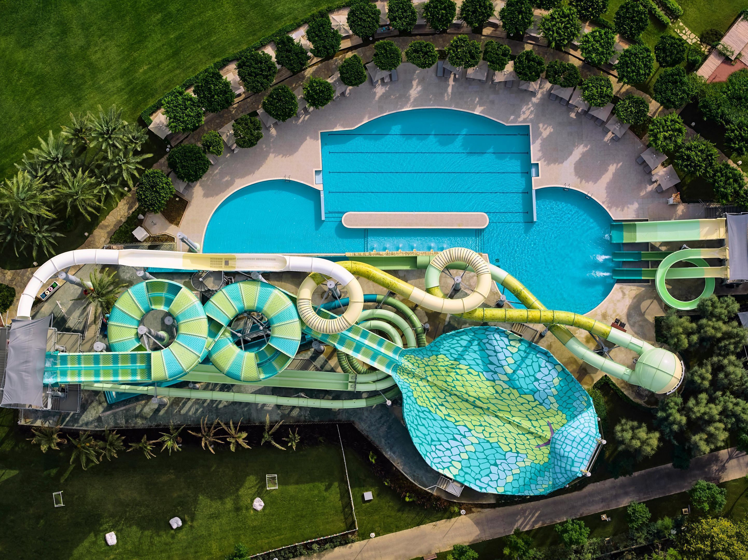 Eine Vogelperspektive eines Wasserparks mit großem Pool, mehreren Wasserrutschen und umgebender Bepflanzung.